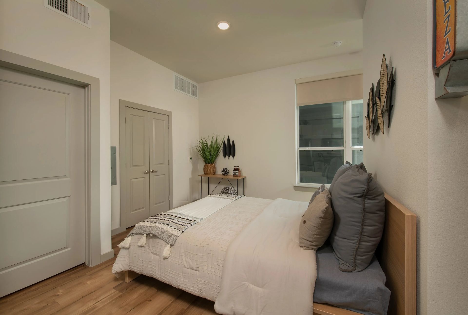 Modern bedroom with a white bed, gray pillows, wood floor, and beige walls