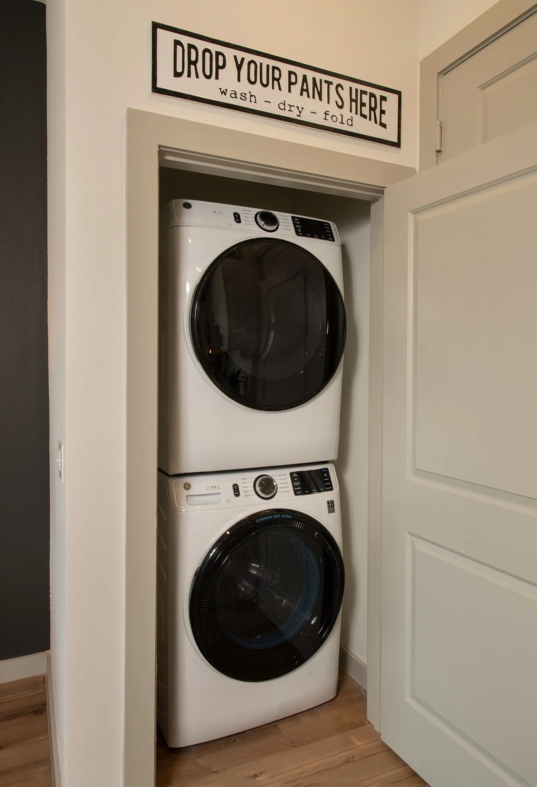 Stacked washer and dryer in a closet under a “DROP YOUR PANTS HERE” sign