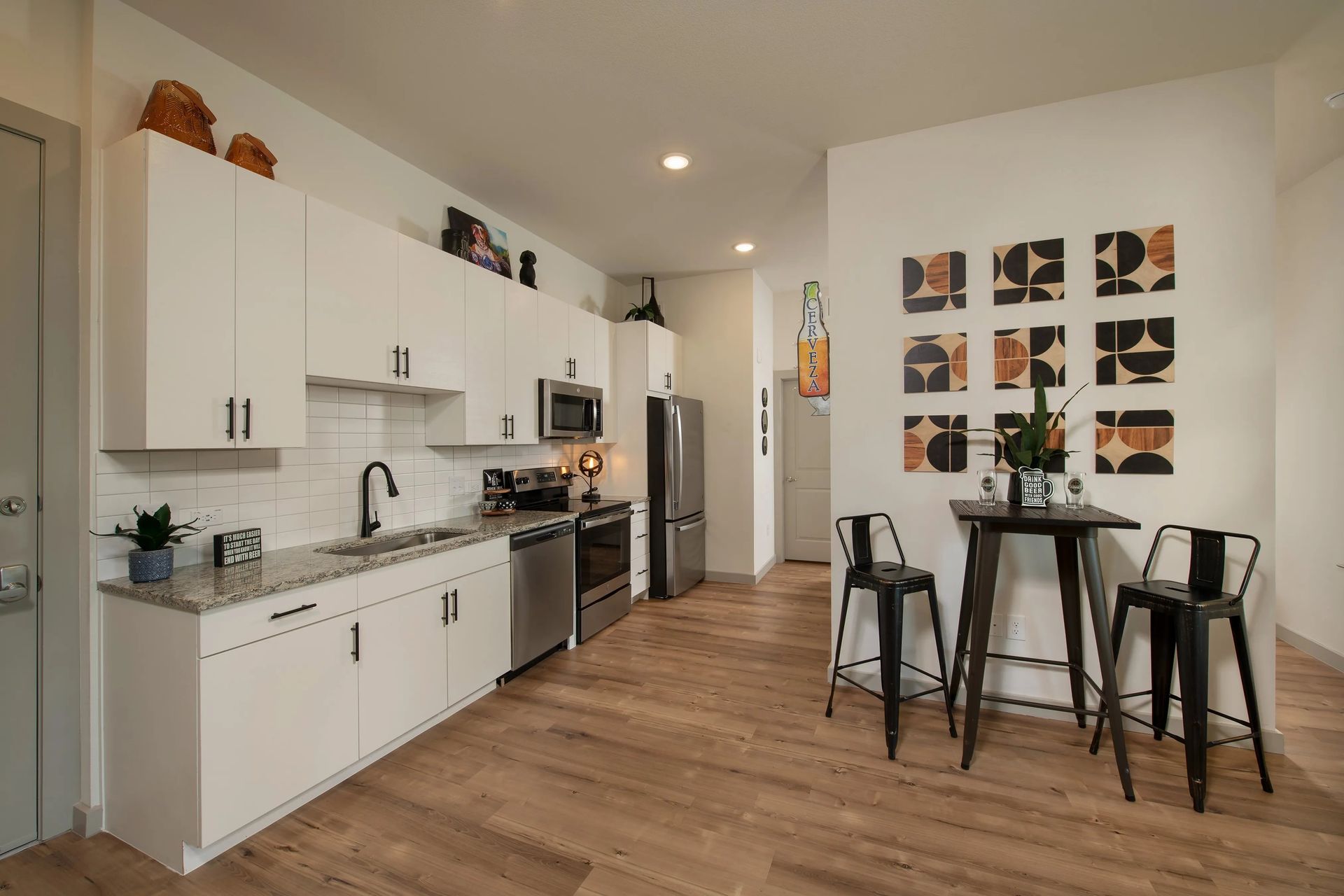 Modern white kitchen with wood floors, stainless appliances, and a small dining table with black chairs
