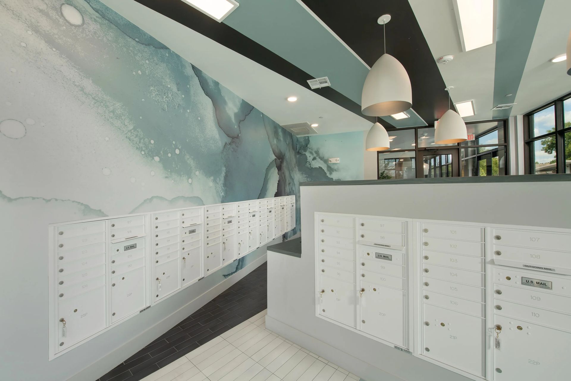 Modern lobby with white mailboxes, teal mural walls, pendant lights, and large windows