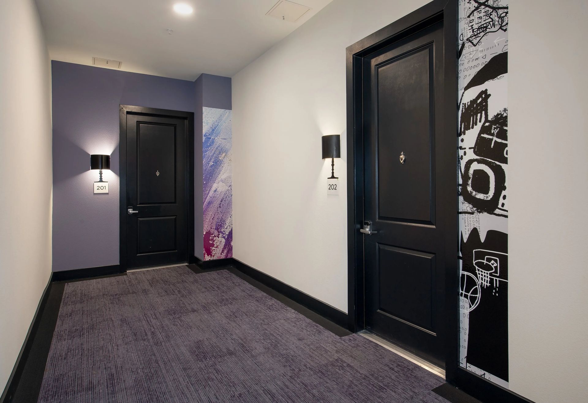 Modern hotel hallway with black doors, wall sconces, and patterned carpet