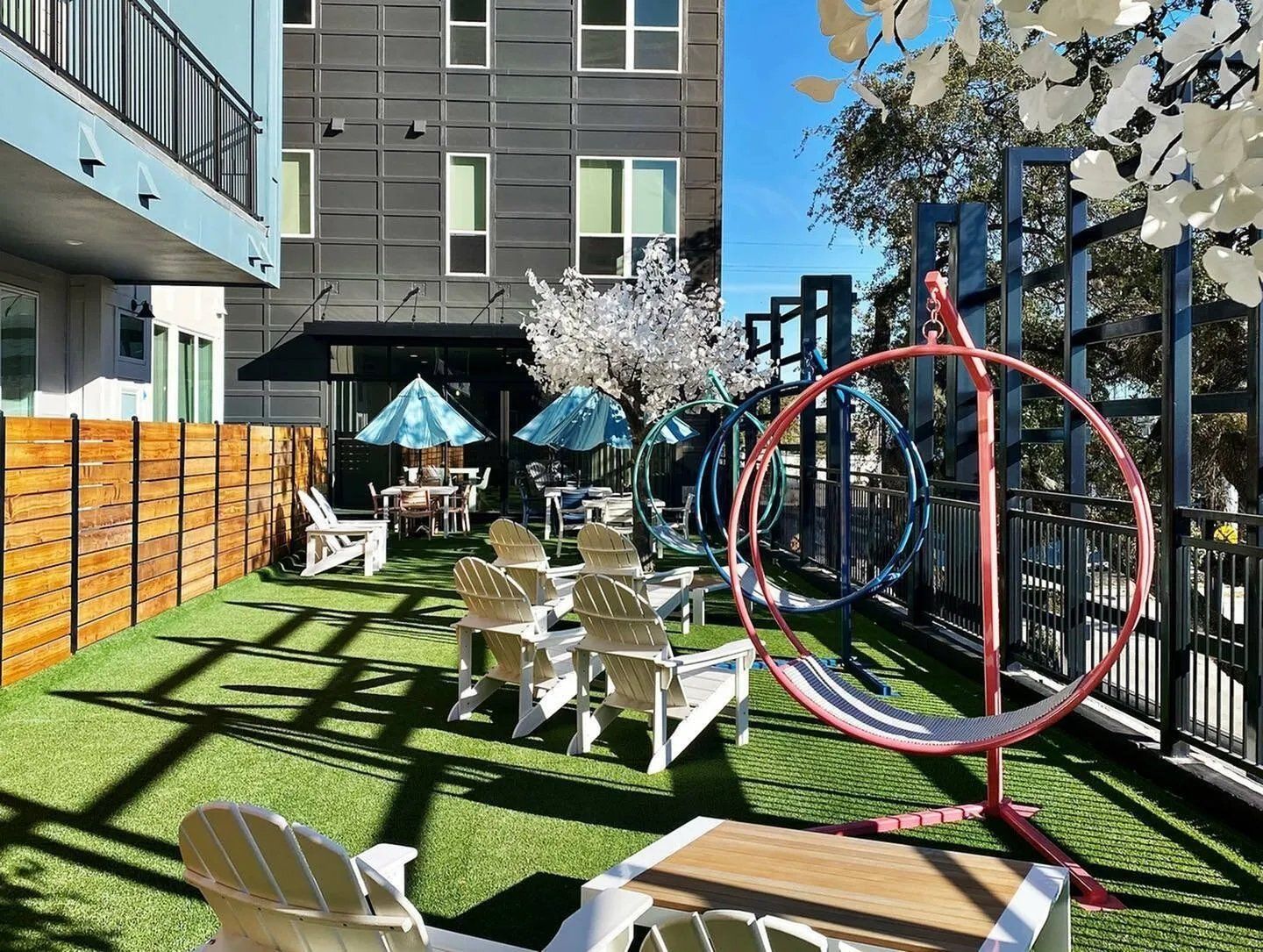 Courtyard with white chairs, turquoise umbrellas, green turf, and a red hanging swing under a blue sky