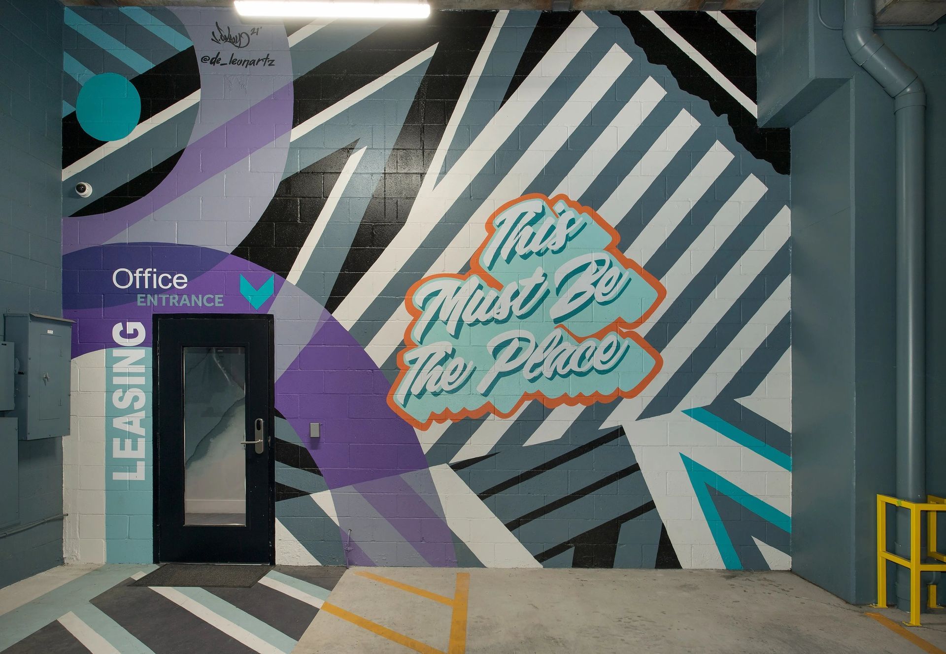 Mural-covered office entrance with bold teal, purple, black, and white geometric stripes and signage.