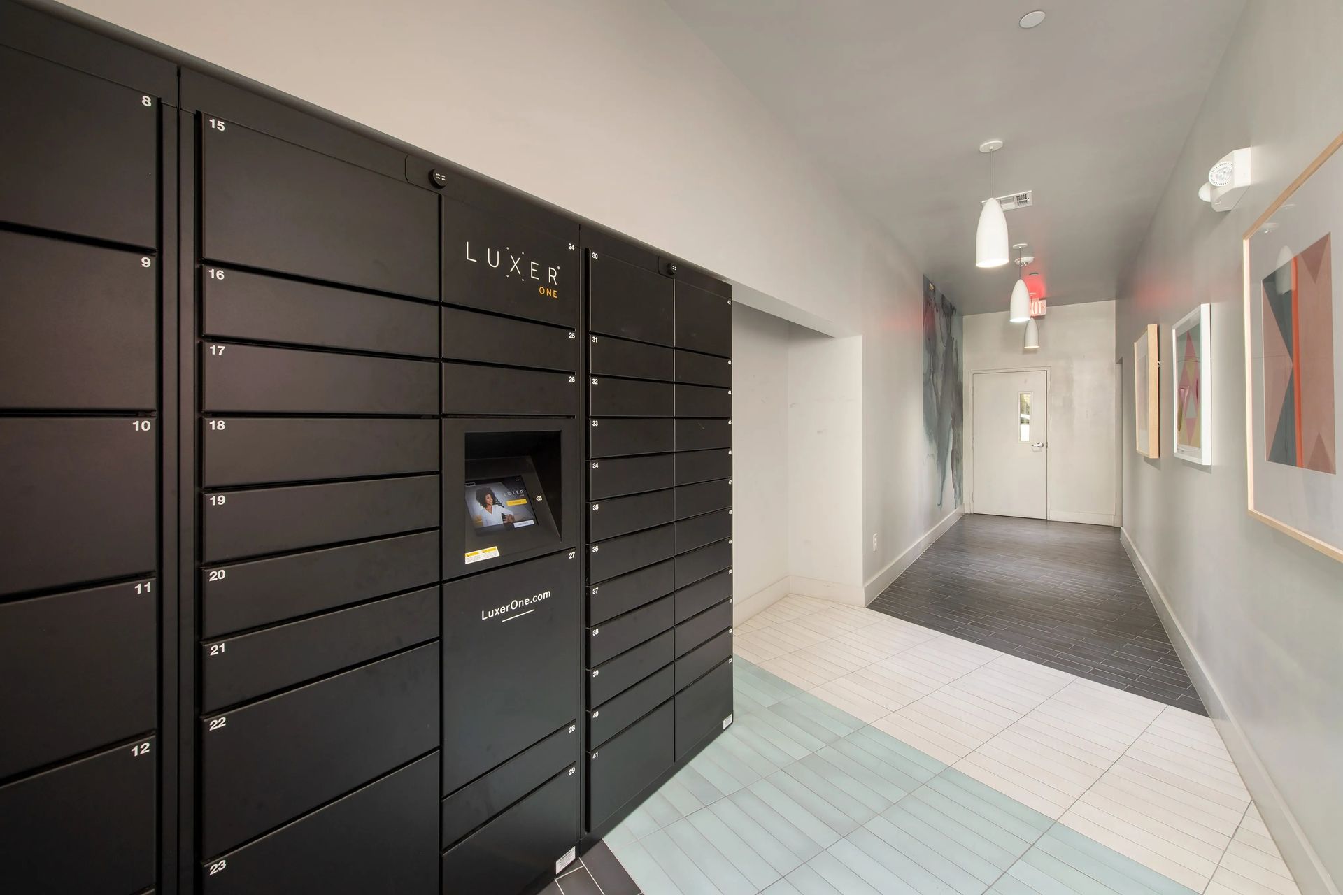 Apartment hallway with black mailboxes on the left and a tiled corridor leading to a bright doorway.