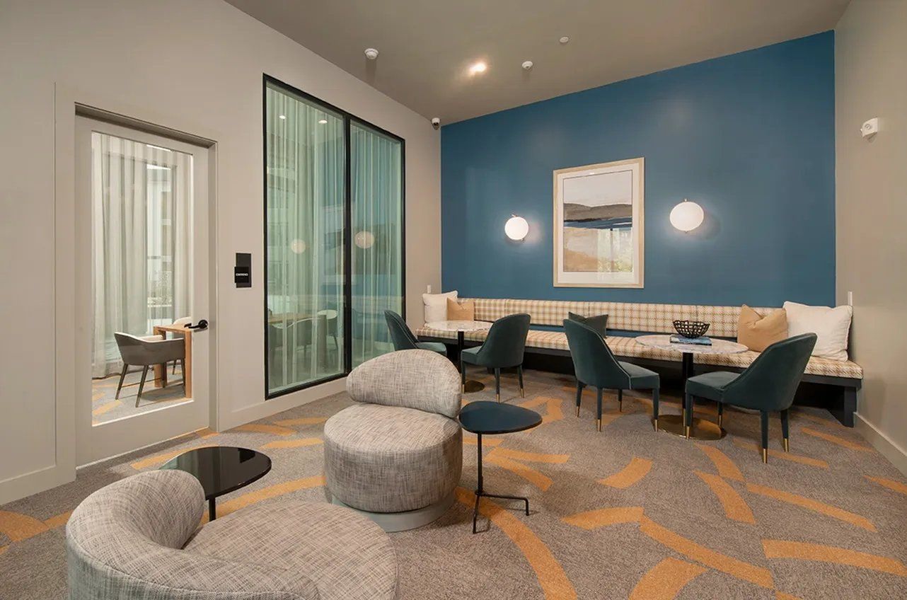Modern lounge with teal accent wall, beige sectional, patterned carpet, and glass doors in a bright office lobby