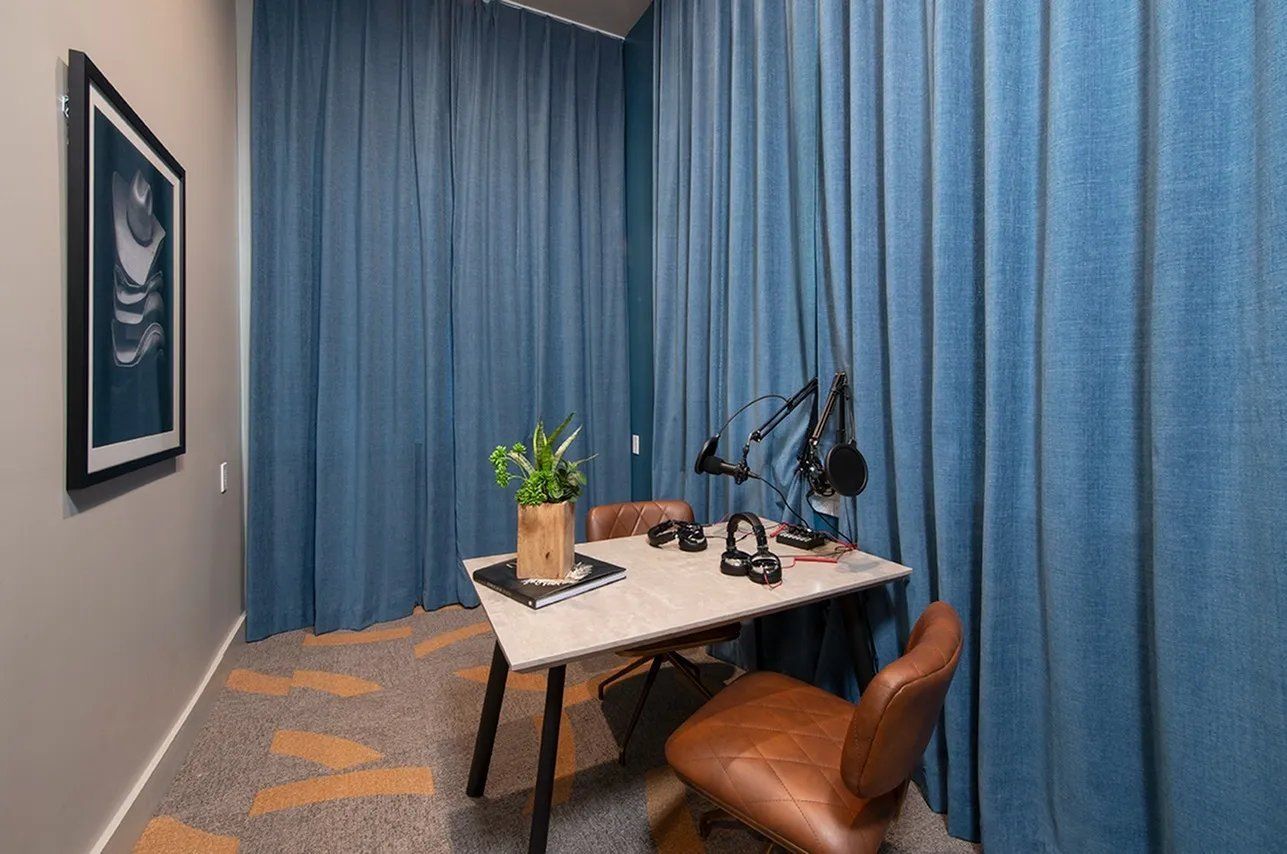 Small office with blue curtains, white desk, brown chair, and potted plant.