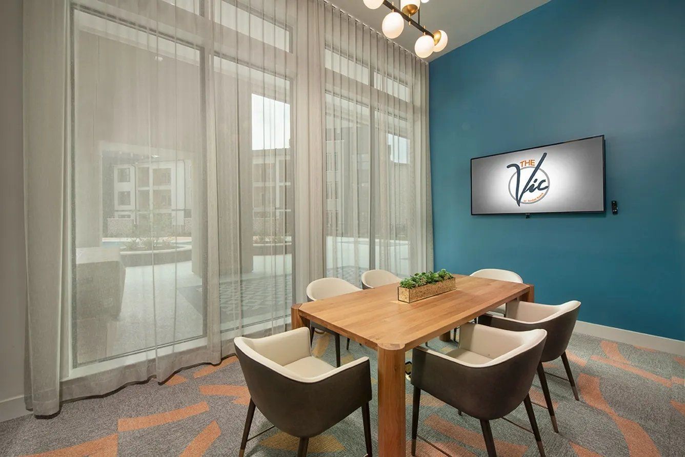 Modern conference room with wooden table, four chairs, blue accent wall, and large windows with sheer curtains