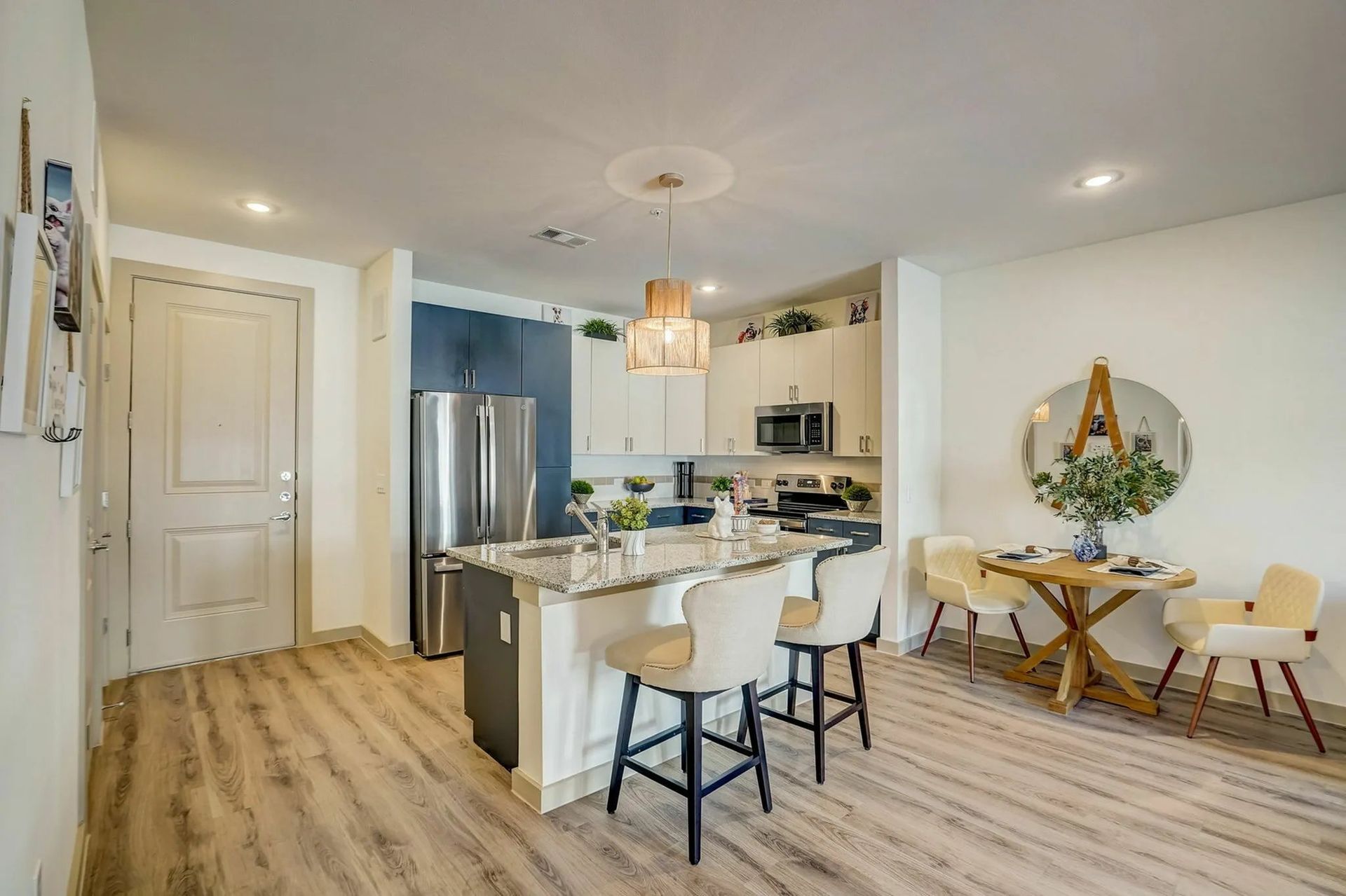 Bright open-plan kitchen and dining area with island, stainless fridge, and rustic table under warm pendant lights