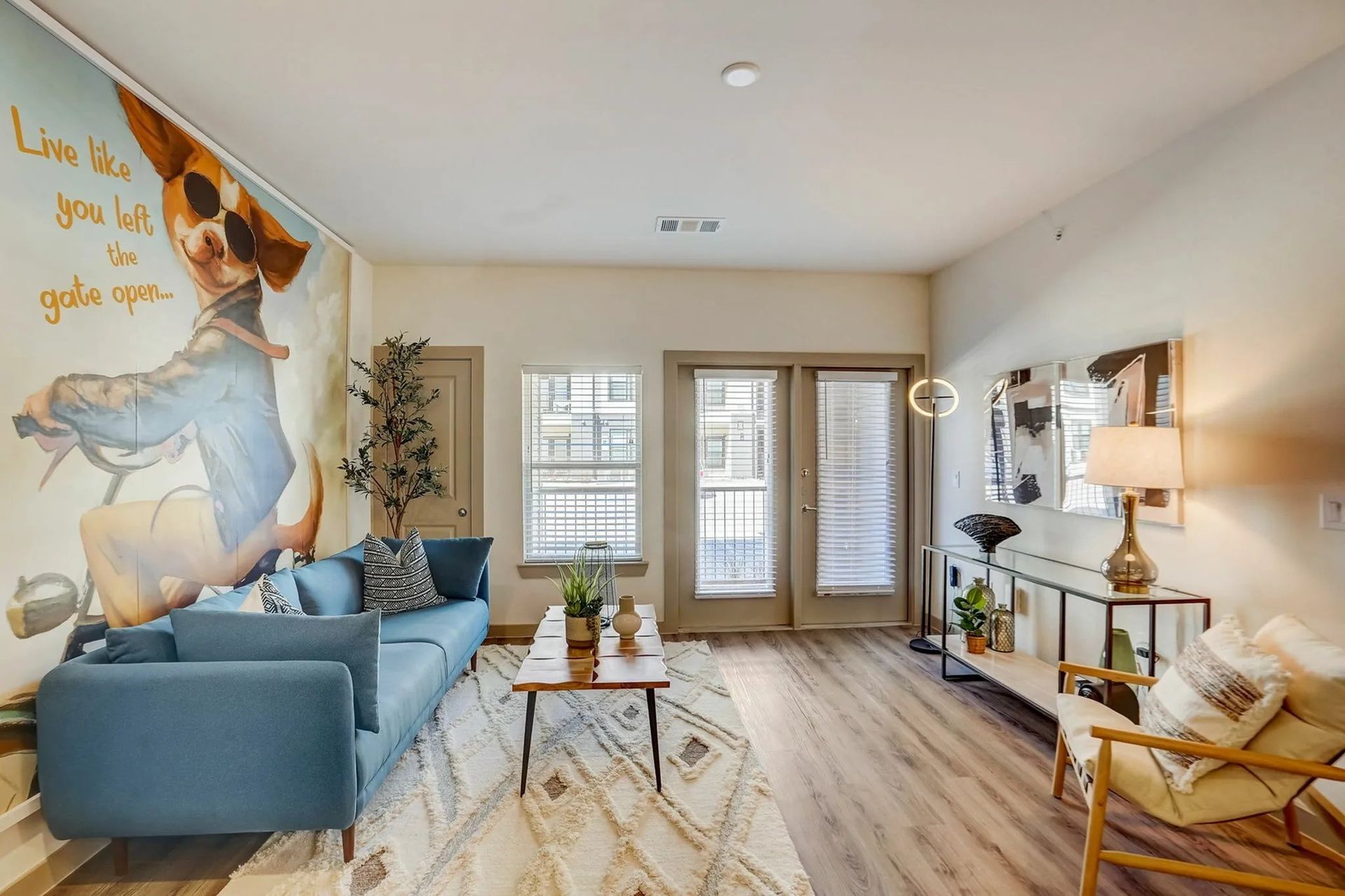Bright living room with blue sofa, mural art, and a TV console by the windowed wall.