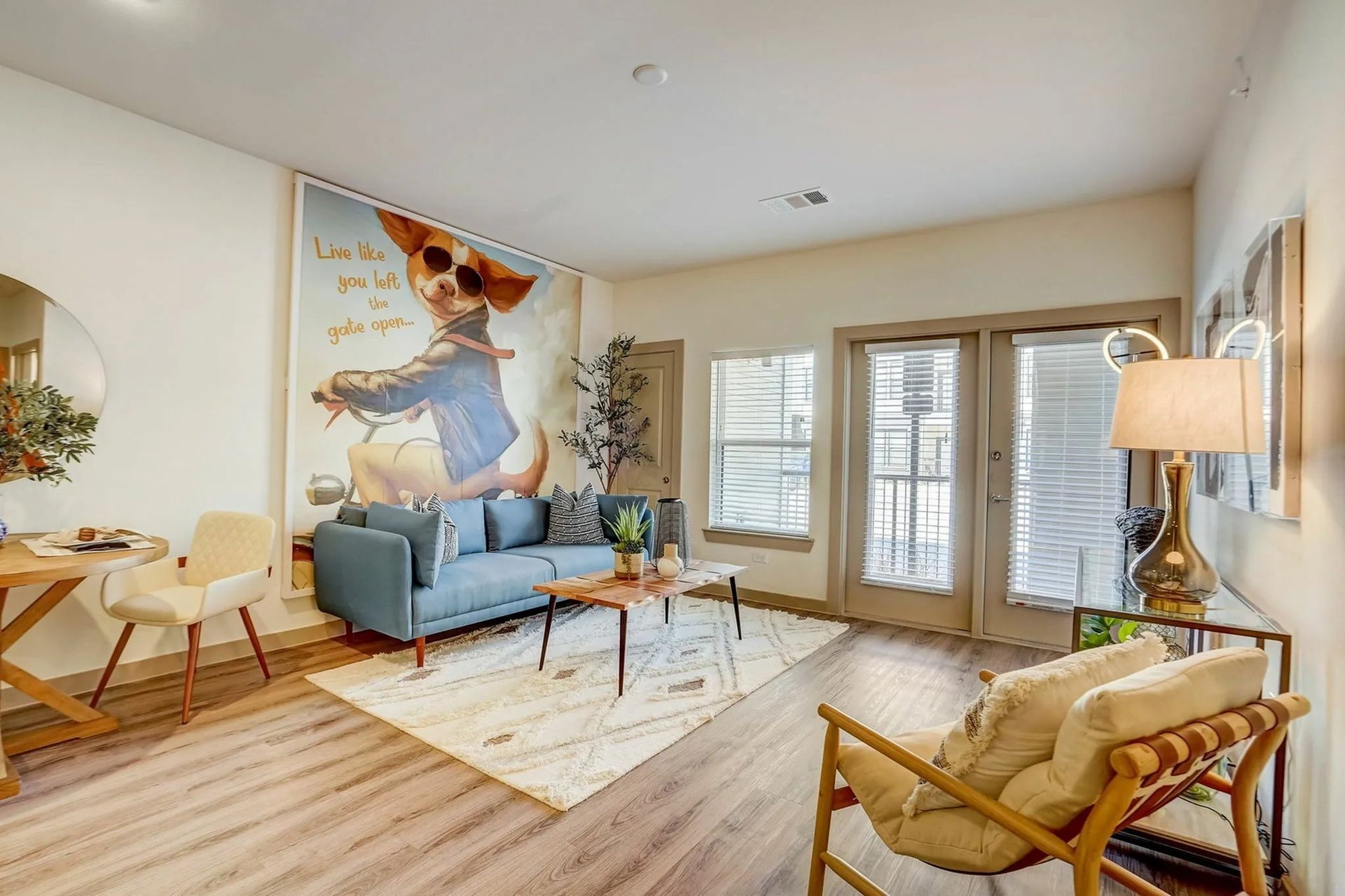 Bright living room with blue sofa, wooden chairs, large wall art, and sliding glass doors to a balcony