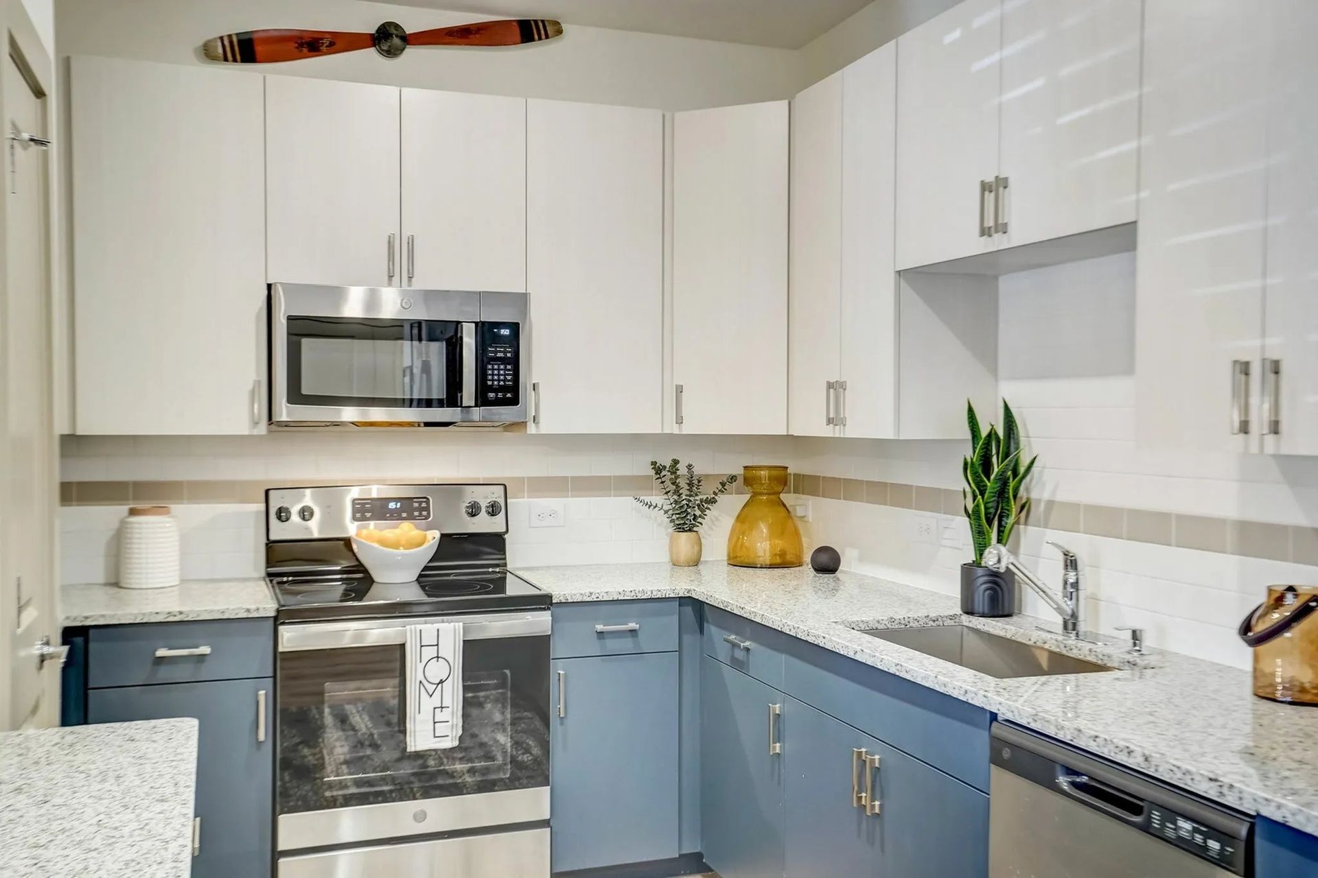 Bright white and blue kitchen with stainless steel appliances and a window over the sink