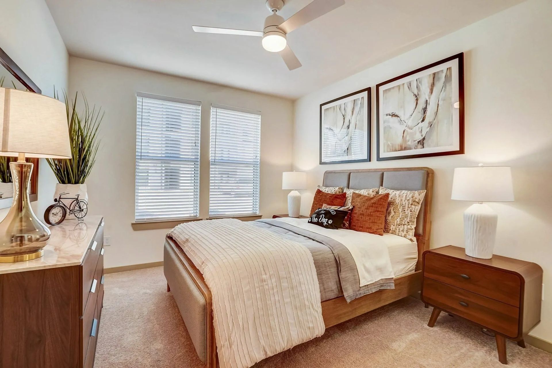 Bright bedroom with a beige bed, wooden nightstands, white lamps, and framed wall art