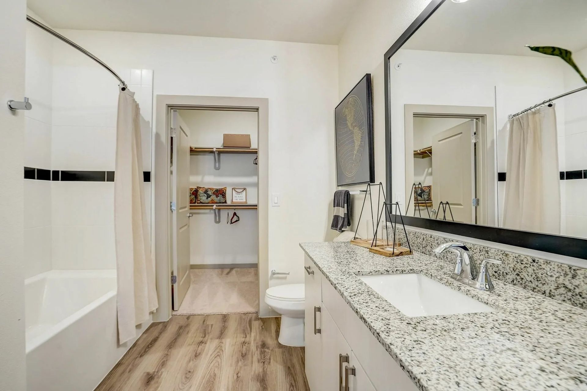 Bright bathroom with double vanity, granite countertop, bathtub, and walk-in closet beyond open doorway