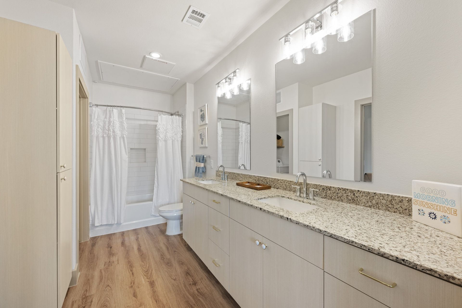 Bright bathroom with double vanity, large mirrors, and a shower curtain over a tub.