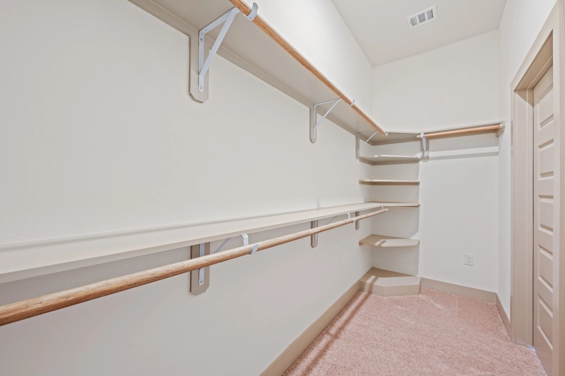 Narrow hallway with white walls, wooden handrails, and a pink carpet leading to a closed door
