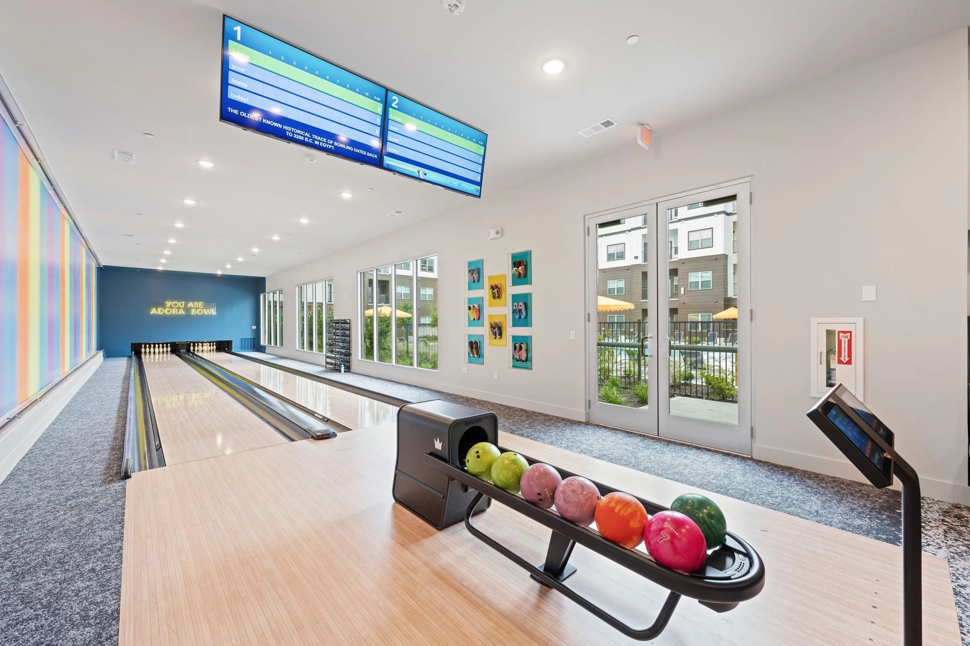 Modern bowling alley with lanes, overhead scoreboards, and colorful bowling balls in the foreground