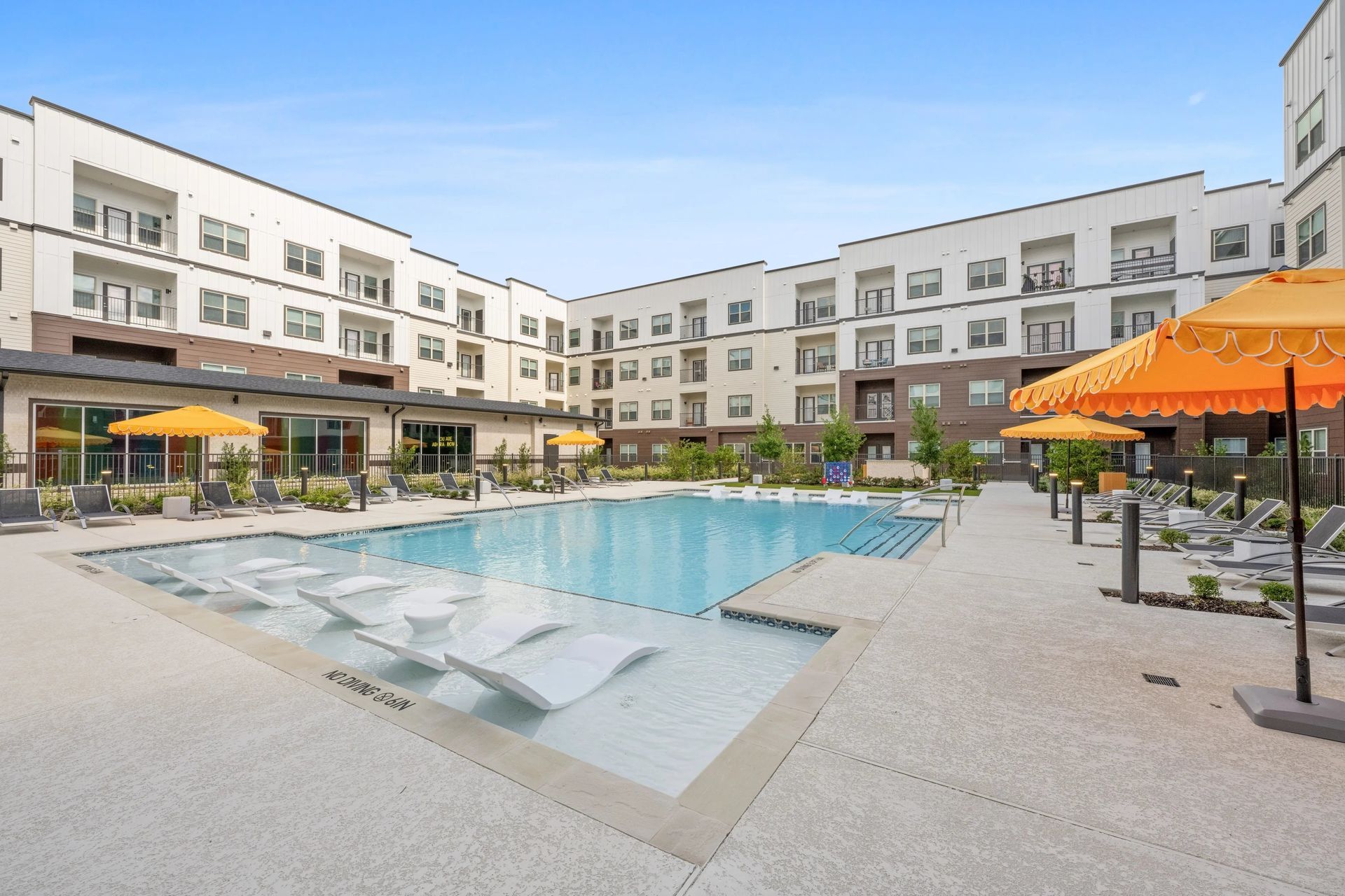 Outdoor apartment courtyard with a swimming pool, lounge chairs, and orange umbrellas.