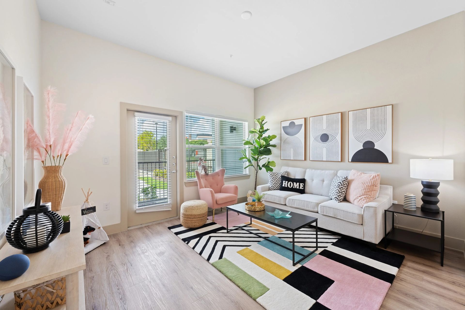 Bright modern living room with pastel decor, white sofa, colorful rug, and large windows