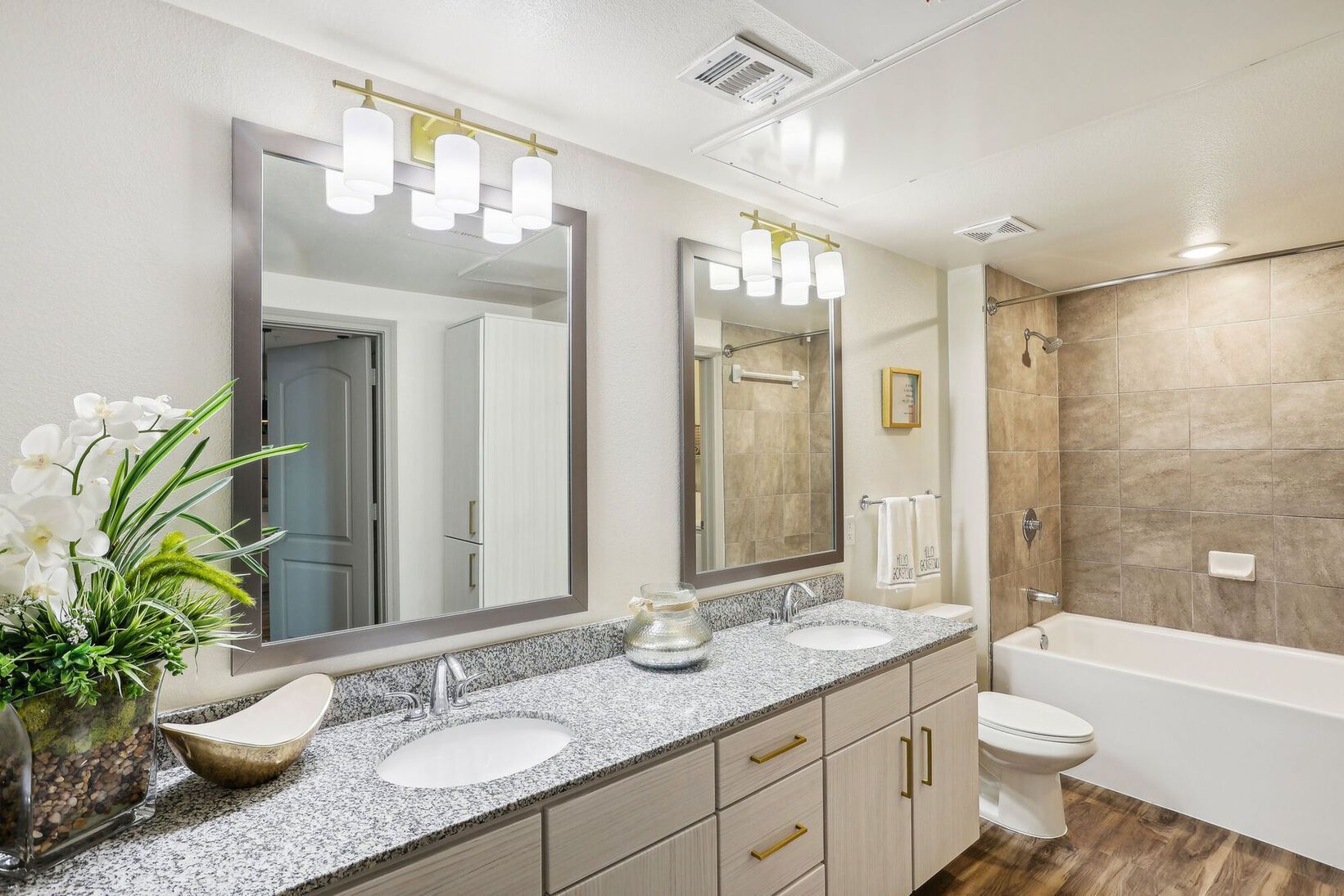 Bright modern bathroom with double vanity, large mirrors, tub, and toilet under vanity lights