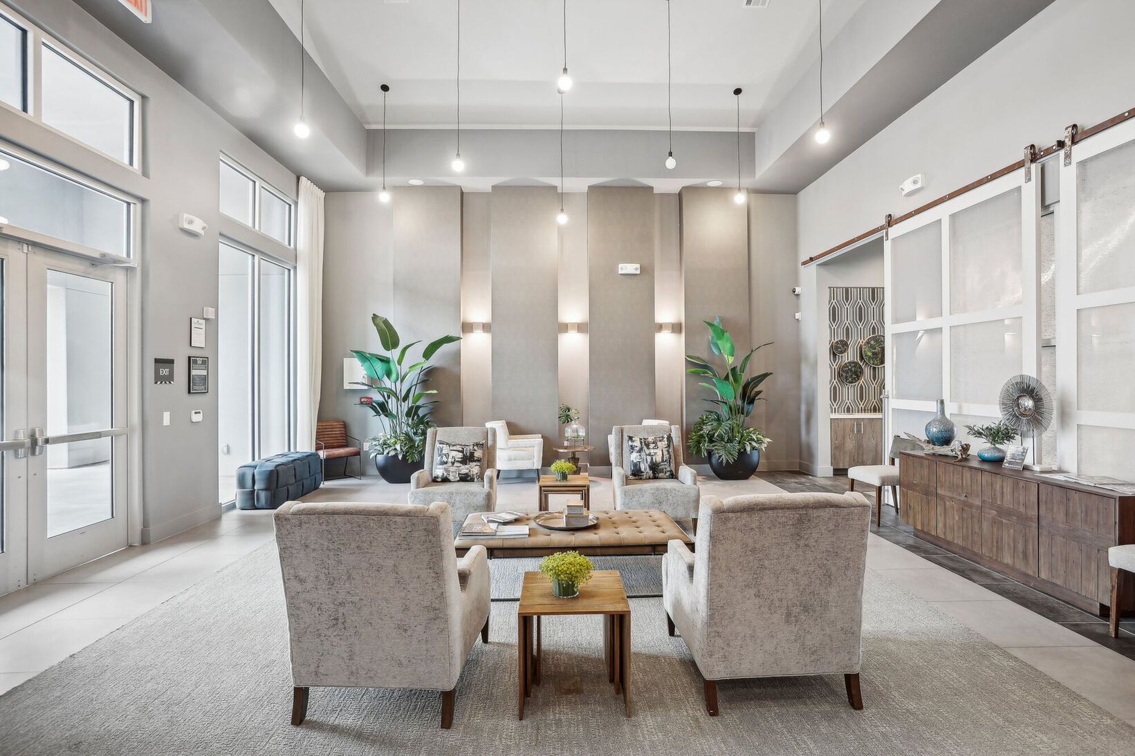 Bright modern lobby with beige chairs, sofa, coffee table, plants, and large windows