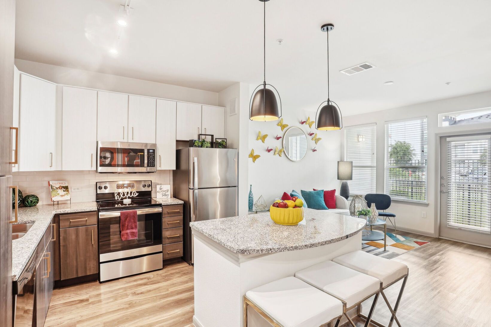 Bright modern kitchen and dining area with white cabinets, stainless fridge, island, and colorful decor.