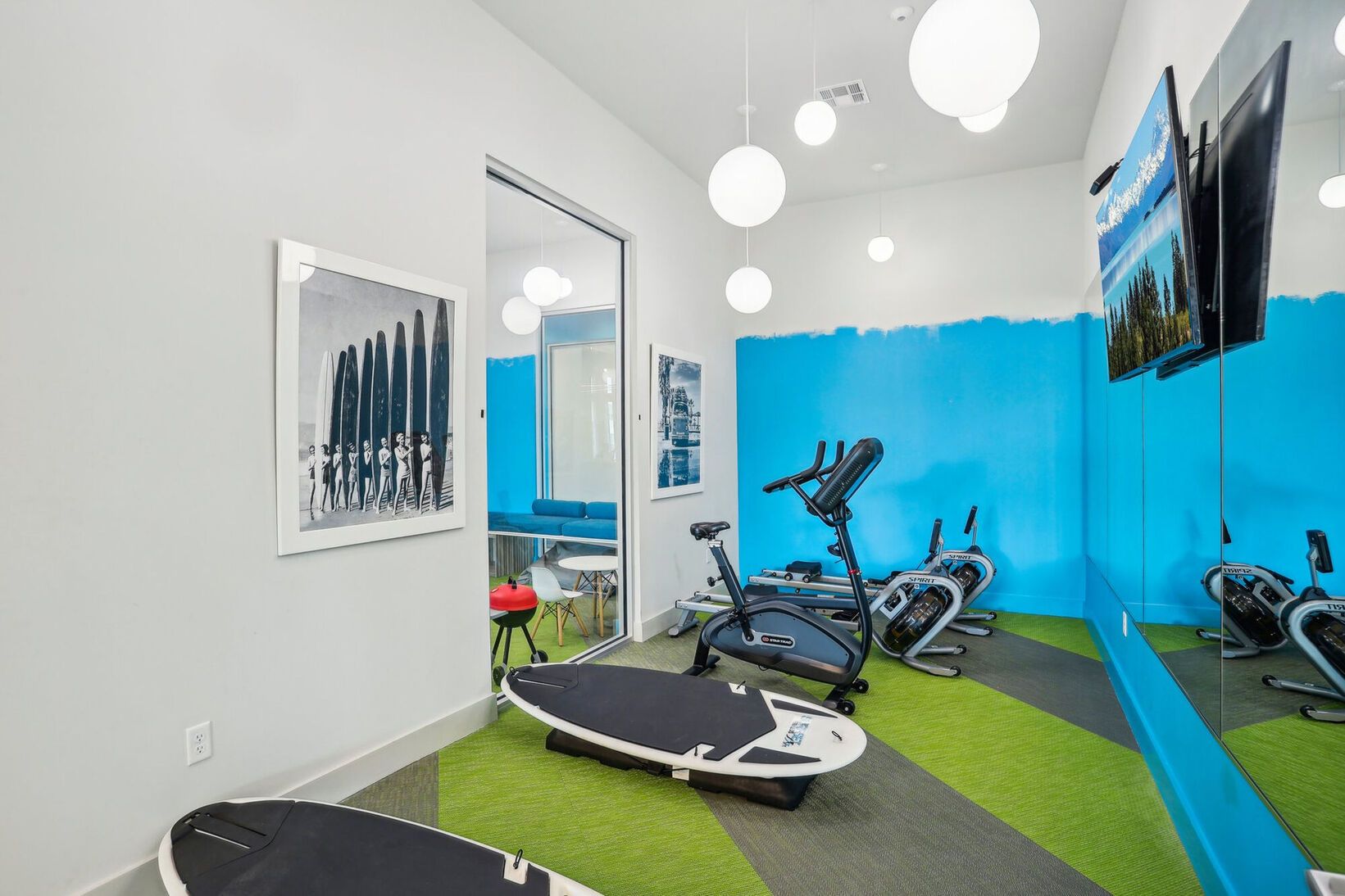 Modern gym room with exercise bike, weights, mirrored wall, and bright blue accent wall