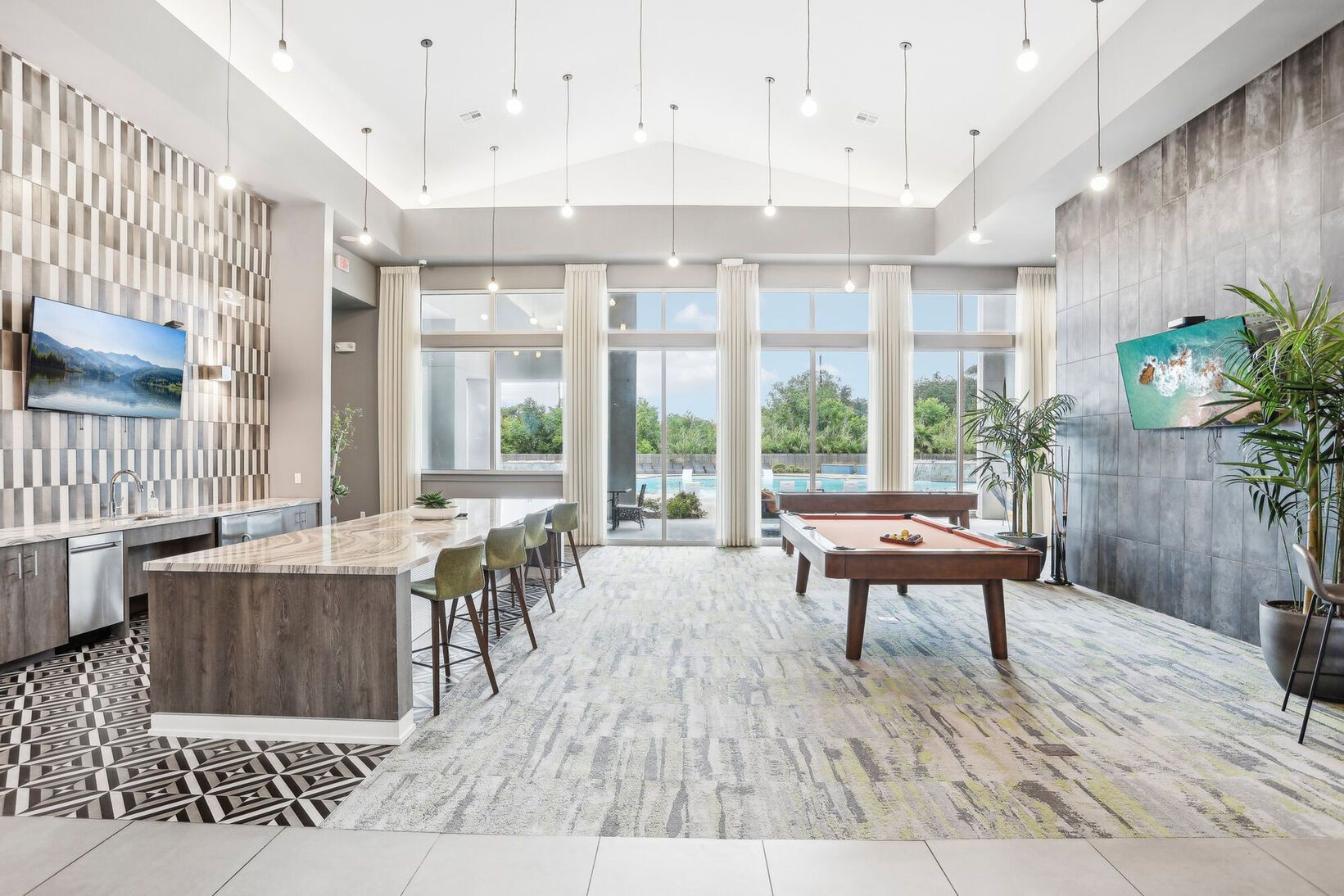 Modern open-concept living room with kitchen island, pool table, large windows, and neutral decor
