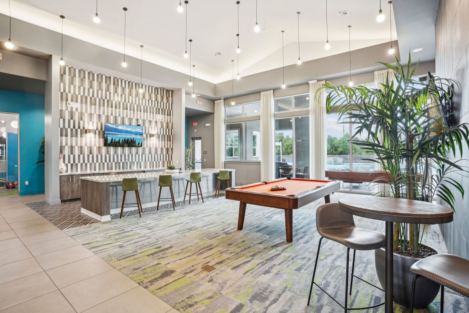 Modern hotel lobby with seating, bar stools, hanging lights, and large windows