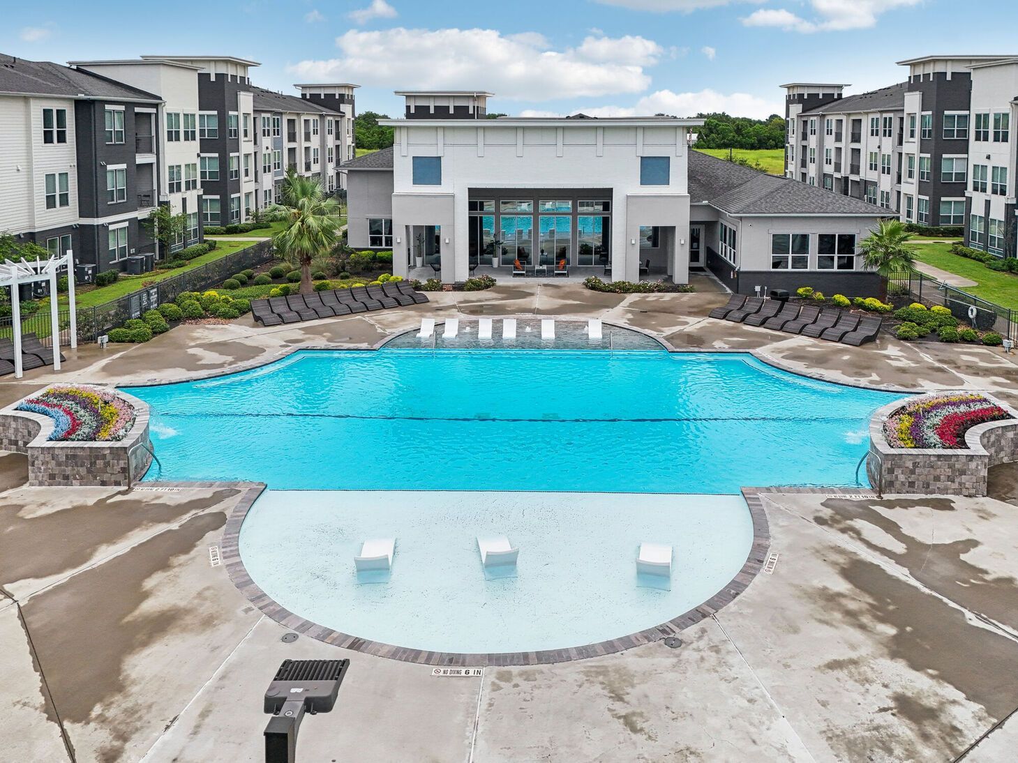 Apartment complex pool with turquoise water, lounge chairs, and modern buildings around it
