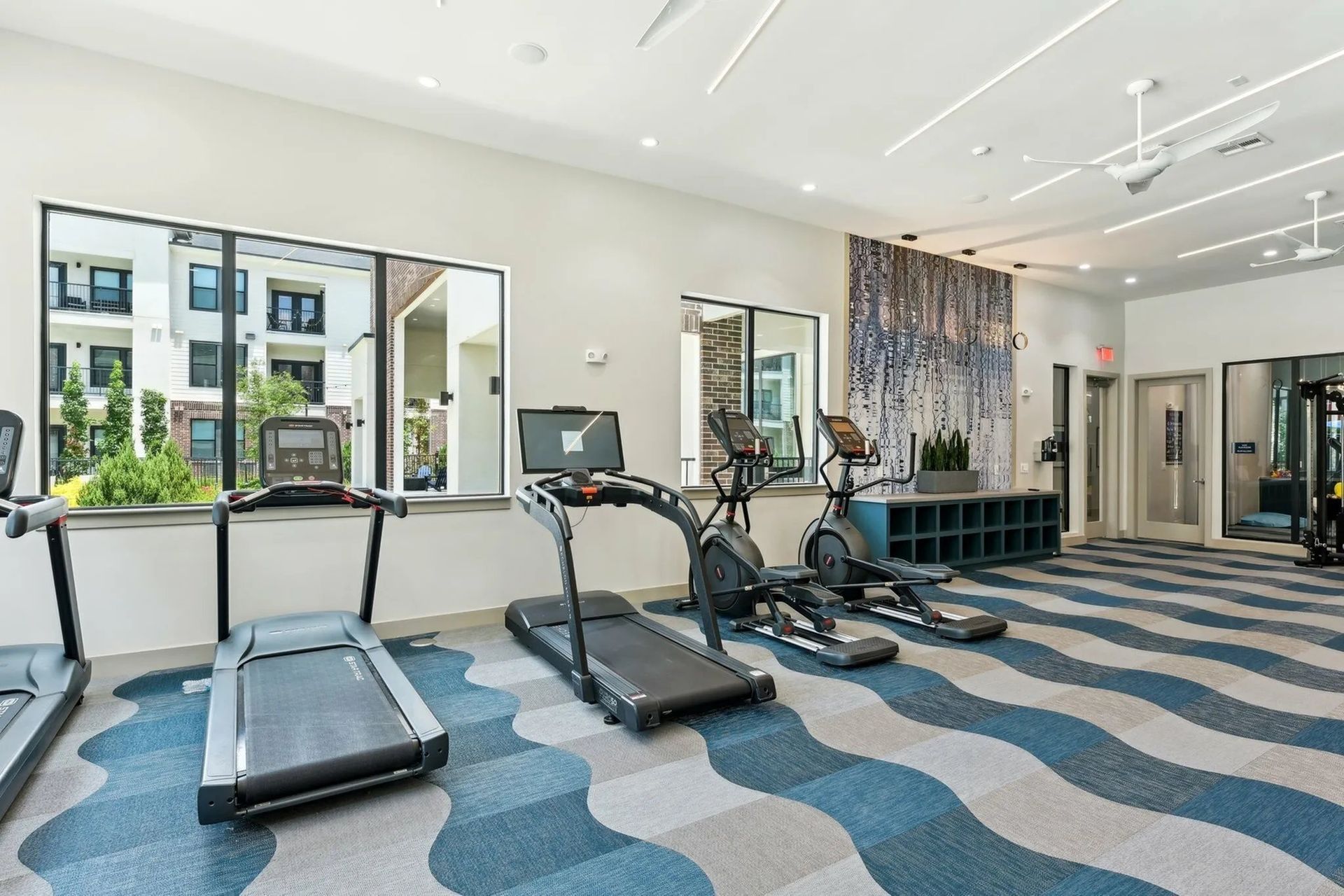 Modern gym with treadmills, elliptical machines, and large windows on a wavy blue carpet