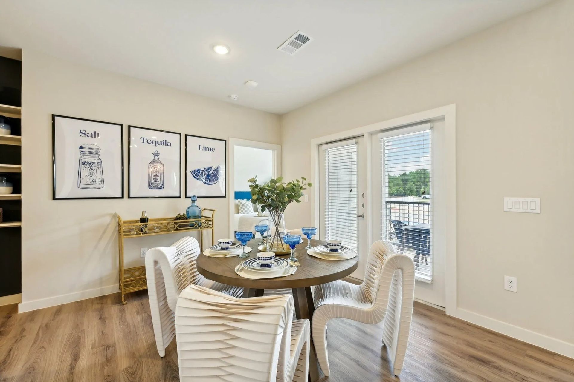 Bright dining room with round table, white chairs, framed art, and French doors to a balcony