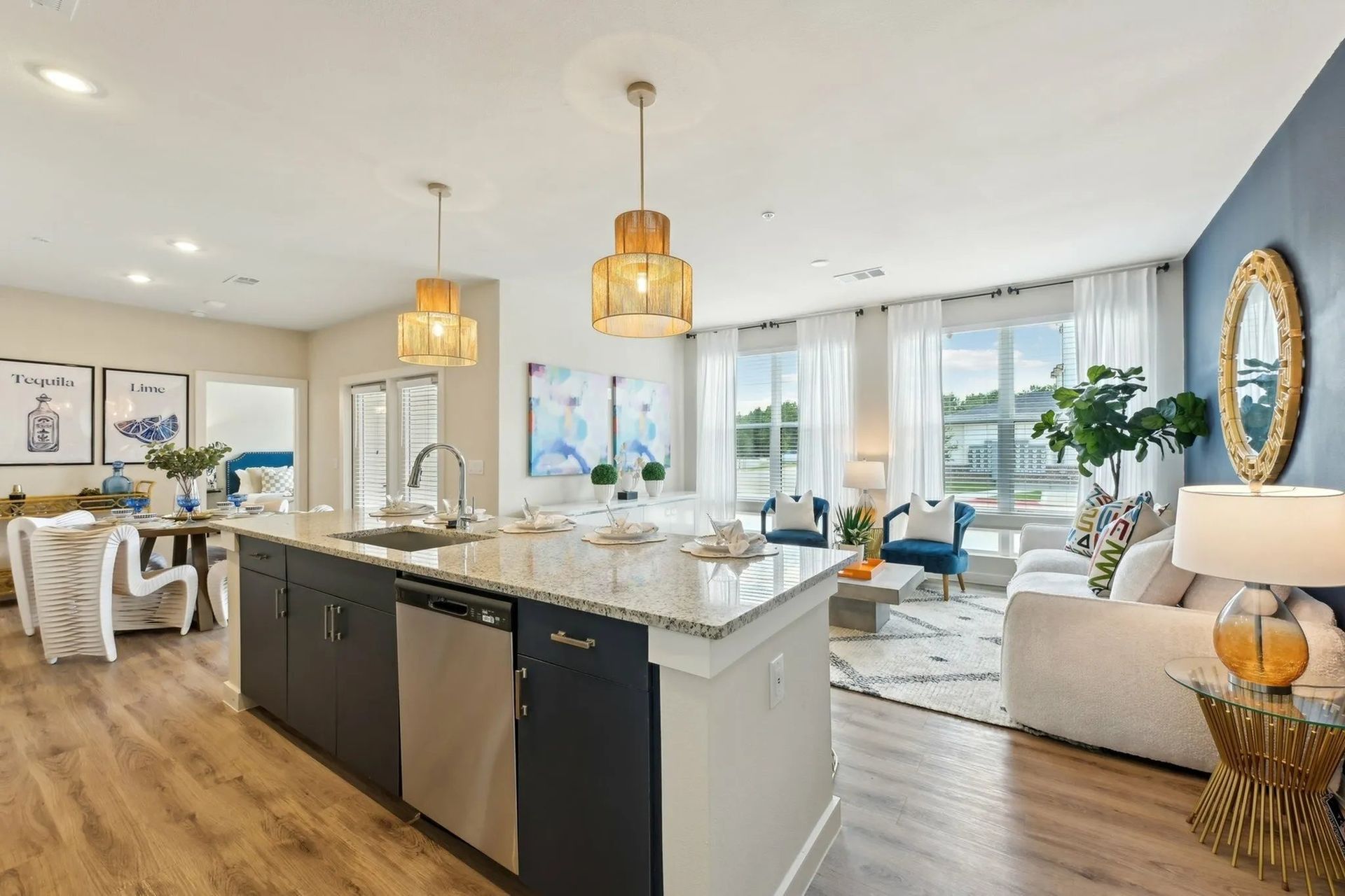 Bright open-concept kitchen and living room with white and blue decor, island, pendant lights, and large windows