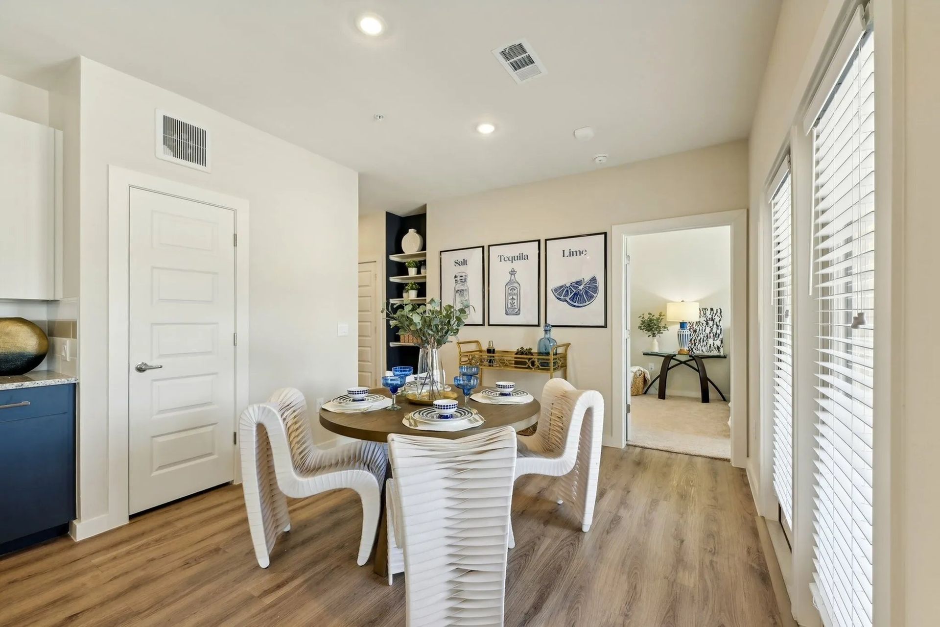 Bright dining room with round table, white chairs, wall art, wood floors, and sliding glass doors.