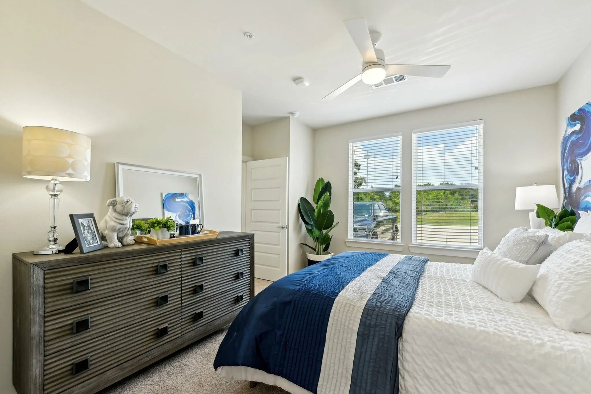 Bright bedroom with a gray dresser, navy bedspread, and sliding glass doors to a green backyard