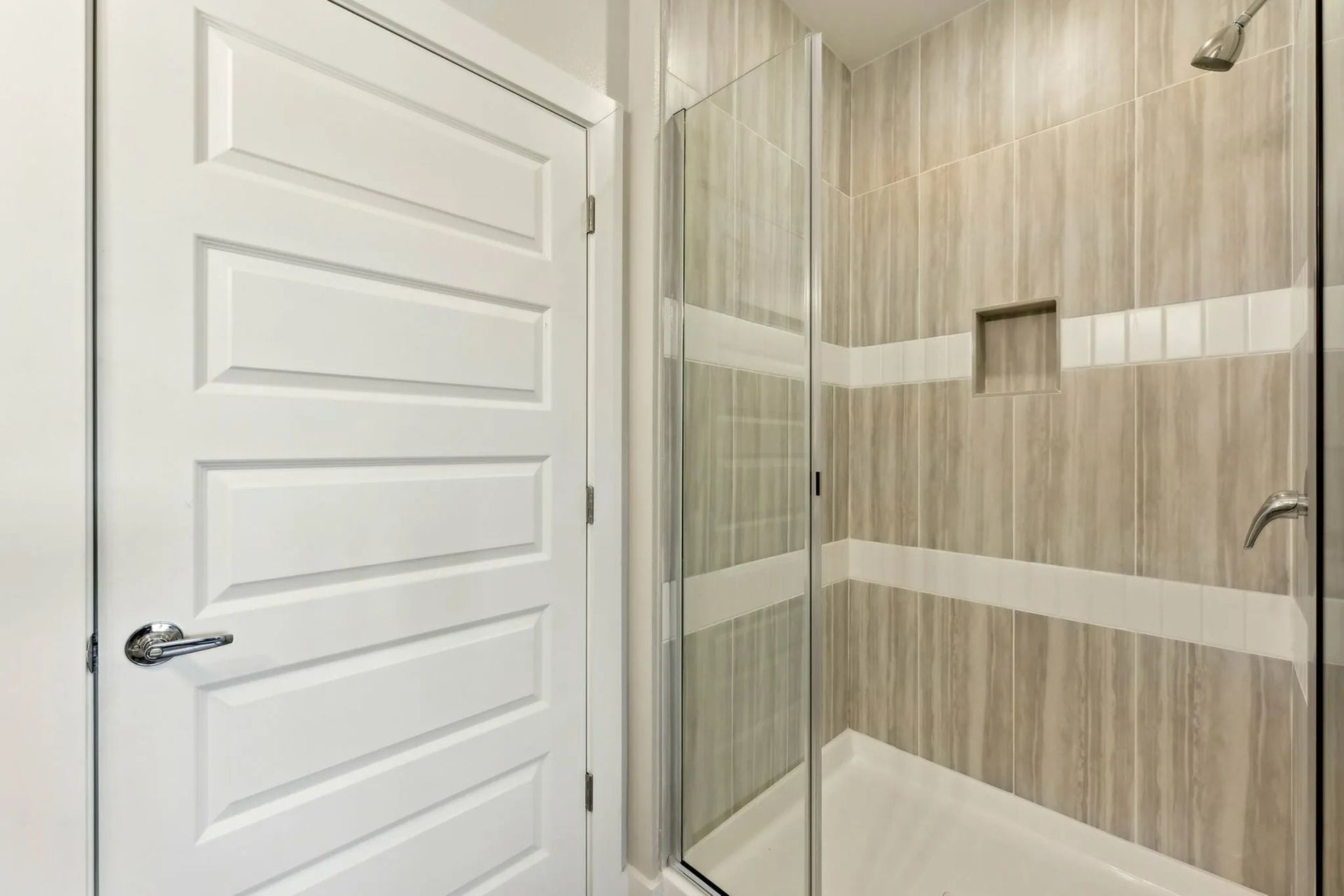 Modern bathroom with white door, glass shower enclosure, and beige tile walls