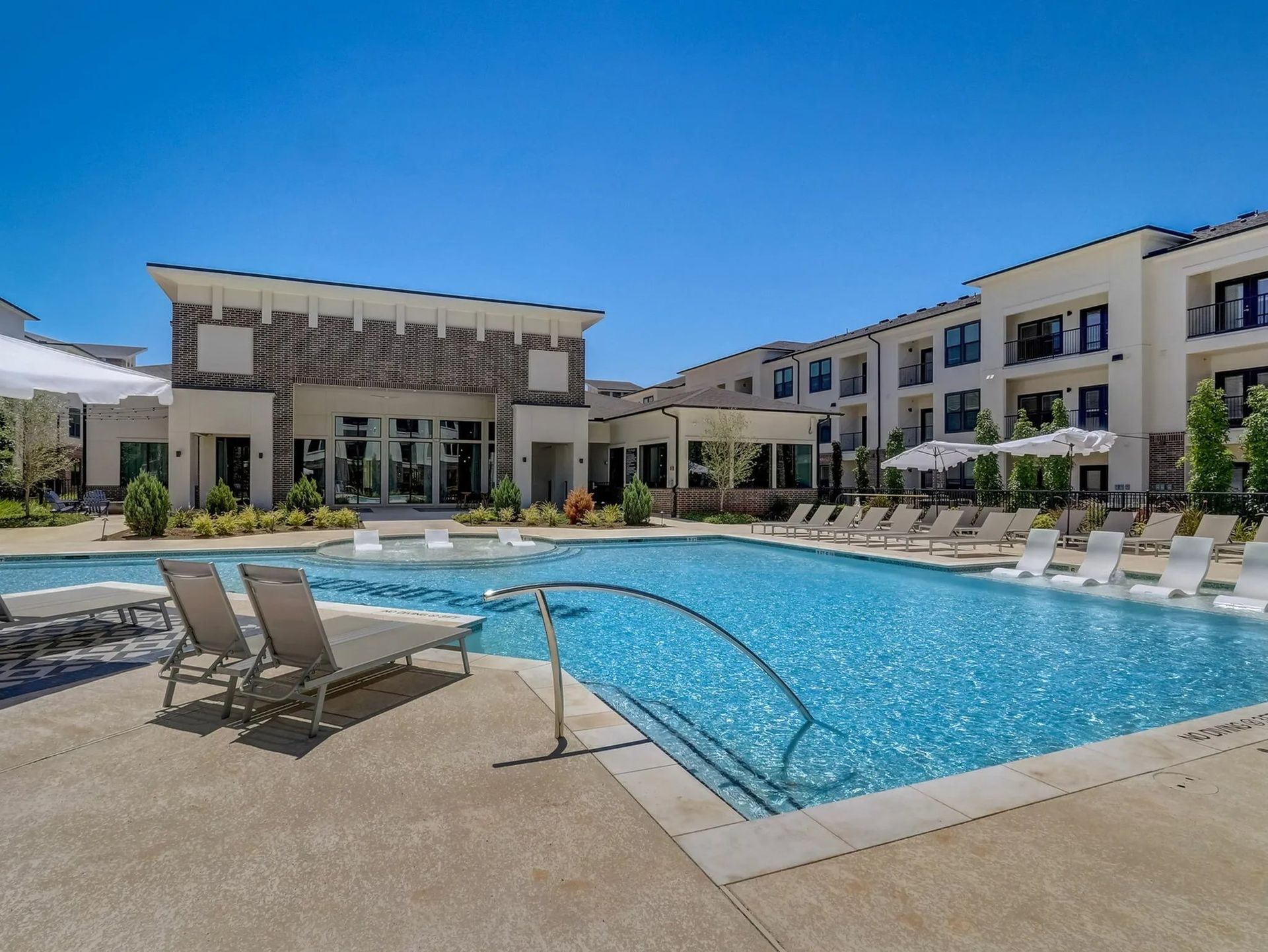 Modern apartment pool courtyard with lounge chairs and clear blue water under a sunny sky