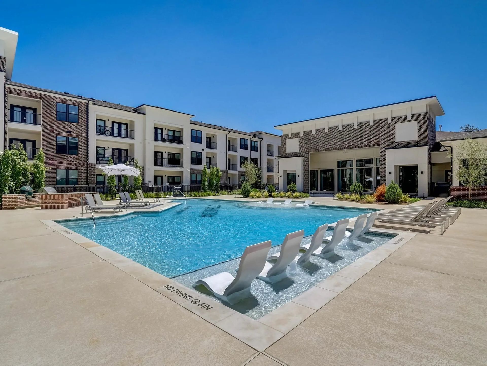 Apartment courtyard with a blue swimming pool, lounge chairs, and modern brick buildings