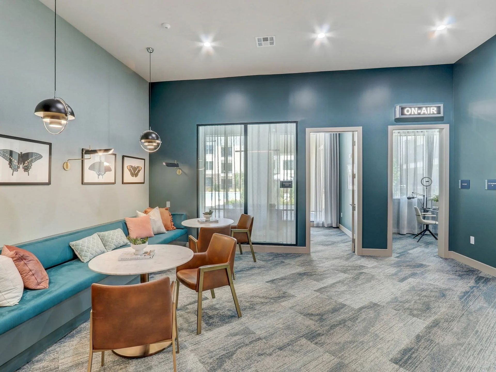 Modern waiting room with teal seating, small tables, wall art, and restroom doors in the back