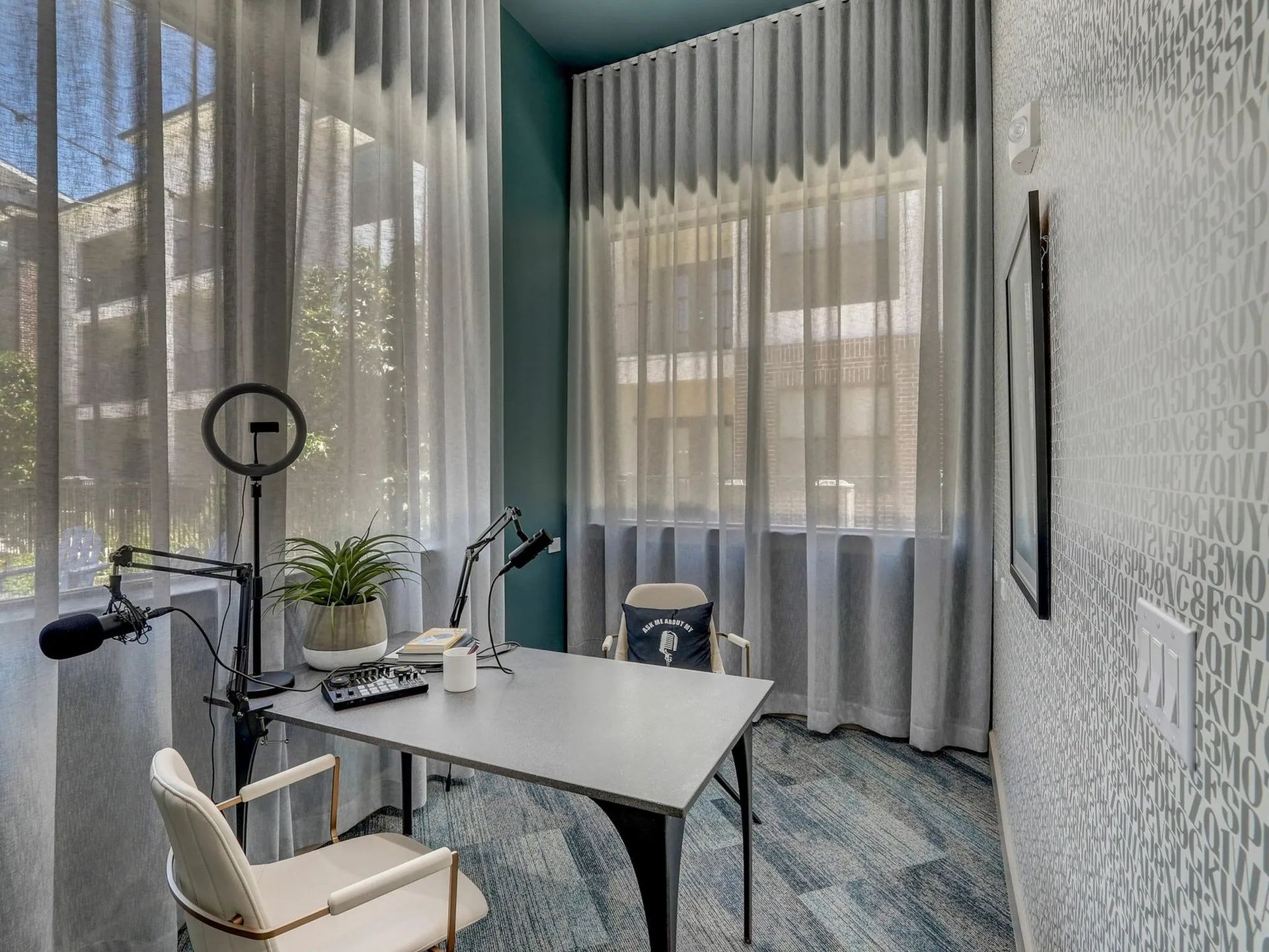 Modern home office with large windows, gray curtains, desk, chair, lamp, and exercise bike in a bright room