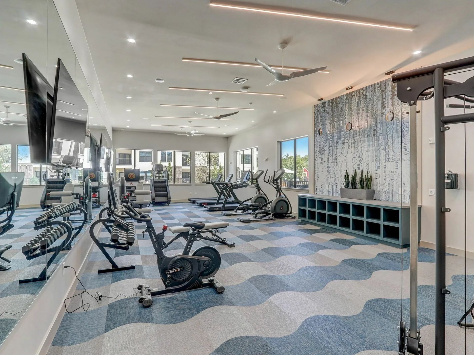 Modern gym with exercise machines, wall mirrors, and blue patterned flooring.