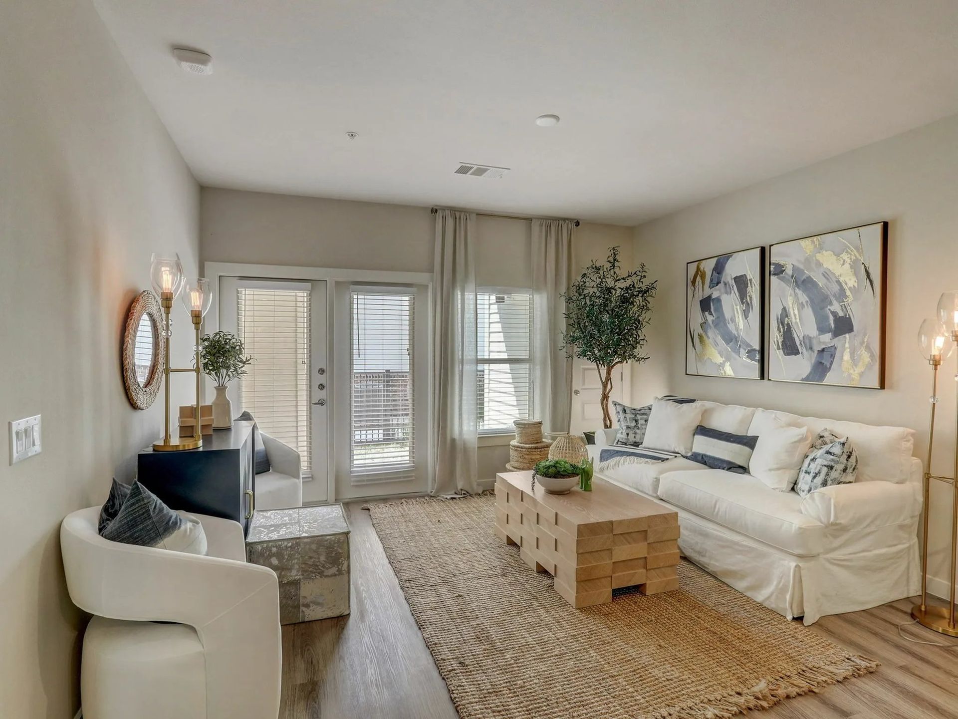 Bright modern living room with white sofa, blue chair, coffee tables, large wall art, and balcony doors.