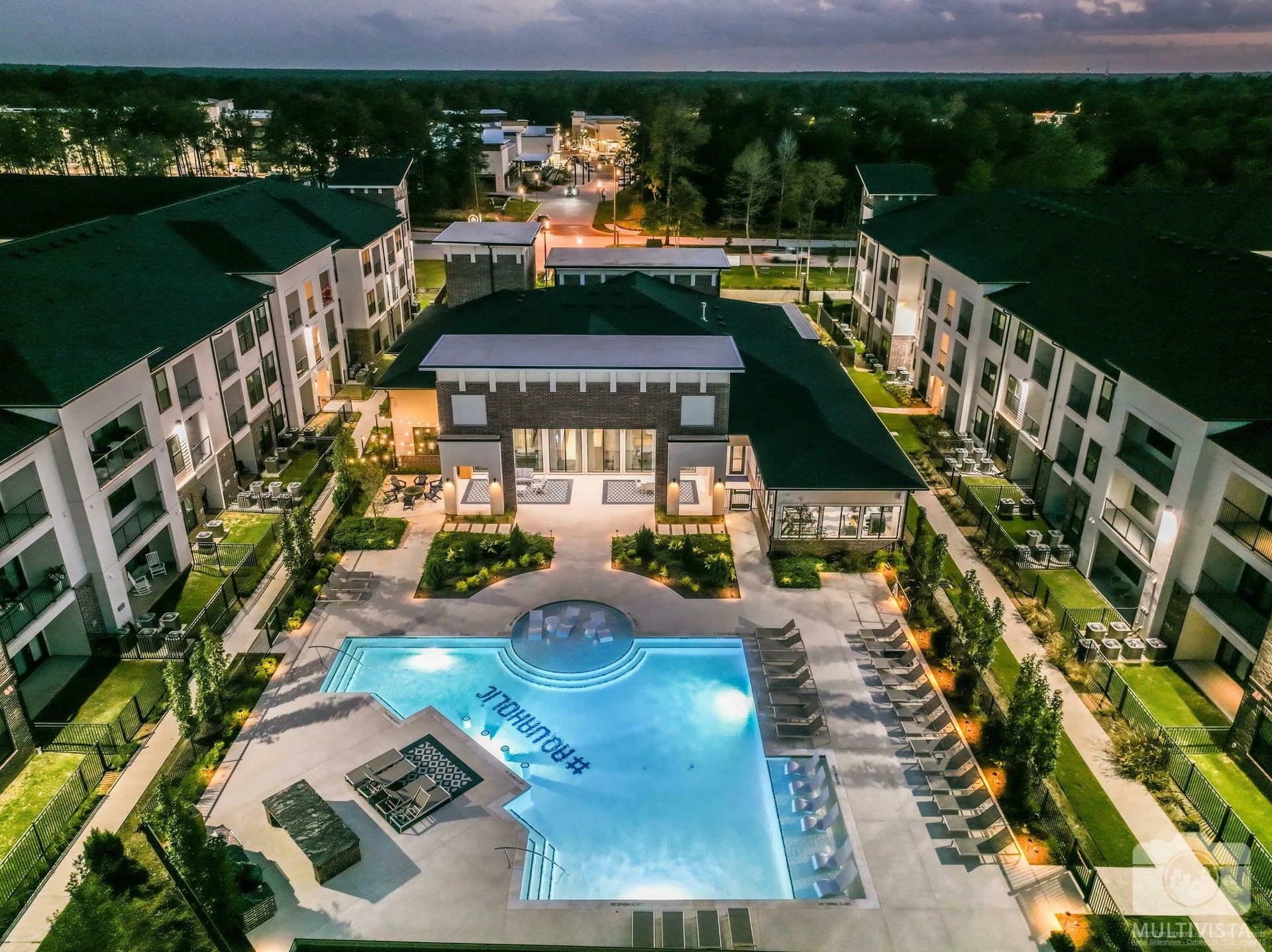 Aerial view of a luxury apartment complex with a lit central pool courtyard at dusk.