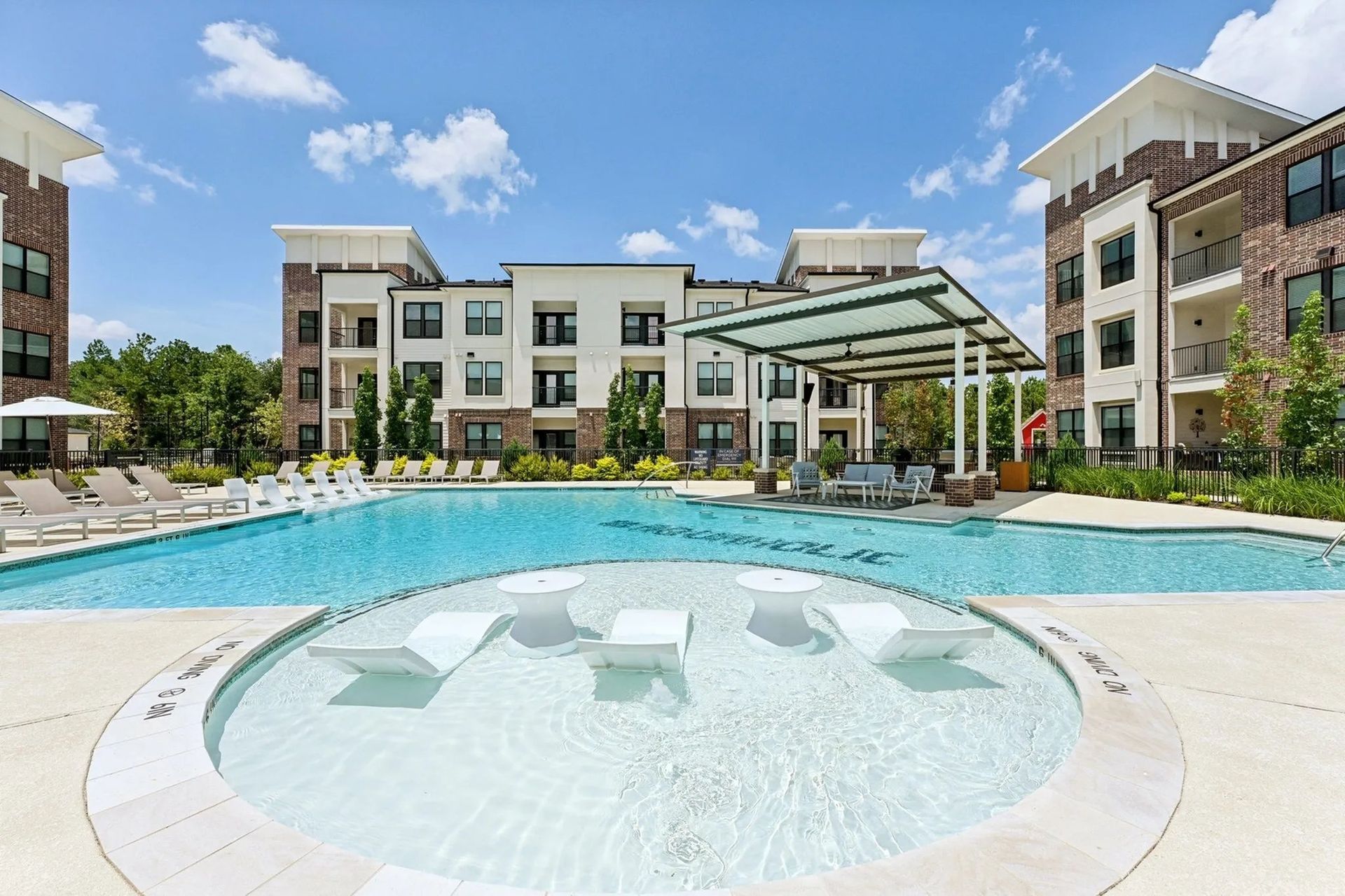 Apartment complex courtyard with a turquoise pool and hot tub under a glass pergola on a sunny day