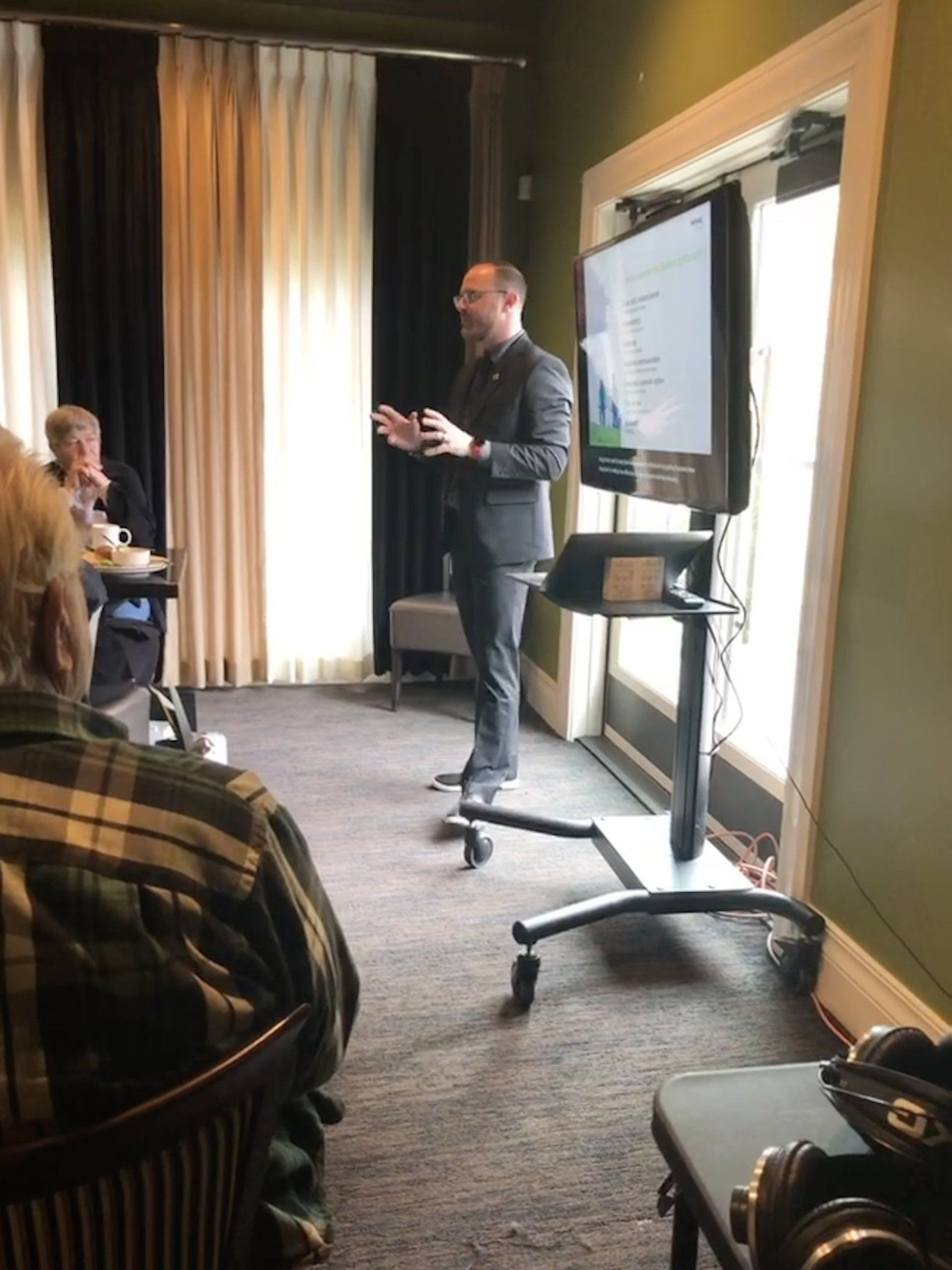 A hearing specialist in giving a presentation to a group of people in a room.