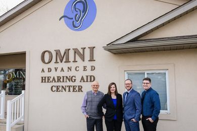 A group of hearing specialist standing in front of a building that says Omni Advanced Hearing Aid Center.
