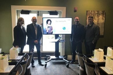 A group of people are standing in front of a large flat screen tv.