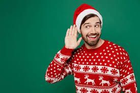 A man wearing a Santa hat and a Christmas sweater is listening to something