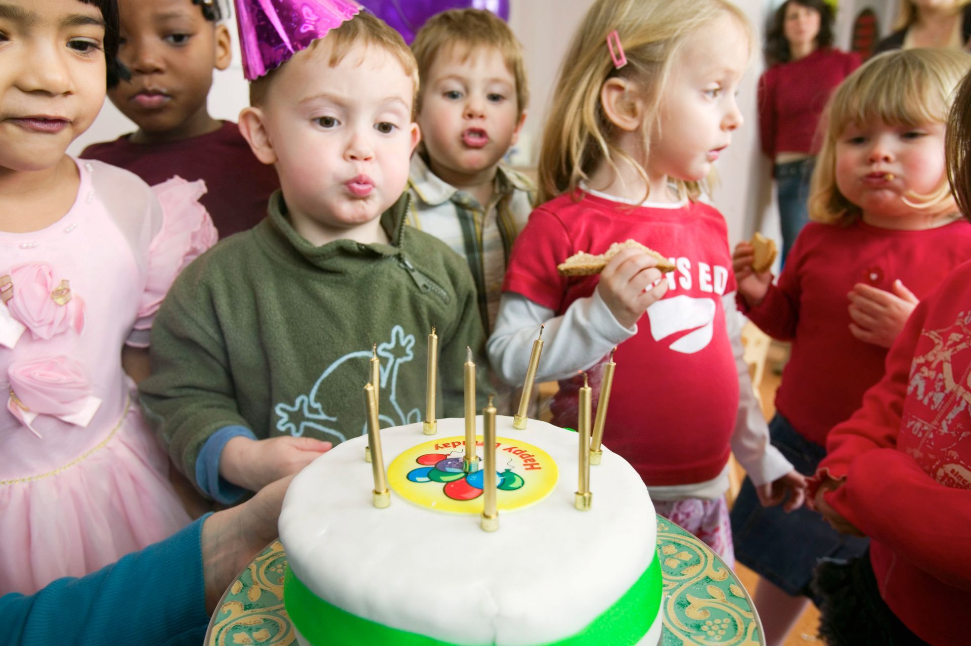 Children blowing out candles on a white cake with a green border; a festive celebration.