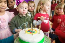 Children blowing out candles on a white cake with a green border; a festive celebration.