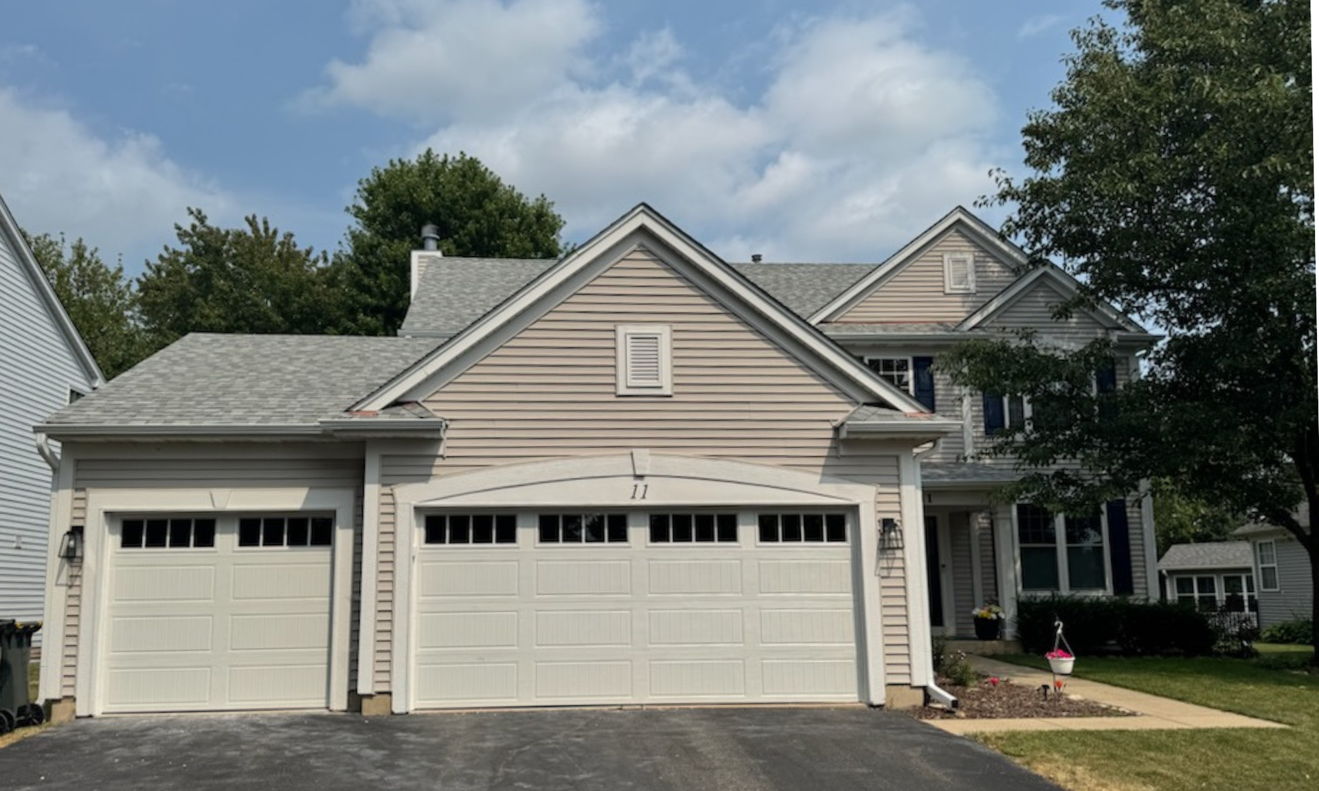 Suburban house with three-car garage and gray-beige siding, viewed from the driveway